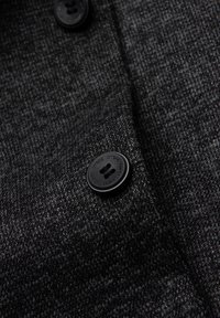 Gros plan sur un tissu noir texturé avec un bouton noir et un motif de tissage subtil. Présente une texture douce et lisse avec des teintes contrastantes.