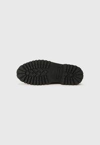 Suela de zapato de goma negra con un patrón de relieve texturizado, que presenta surcos profundos y un área central lisa. Duradera y diseñada para ofrecer tracción.