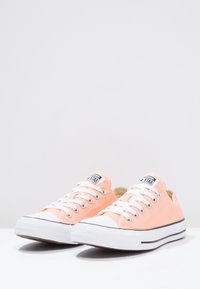 Baskets basses en toile rose avec lacets blancs, embouts en caoutchouc et bandes noires le long de la semelle. Présentent un patch logo sur la languette.