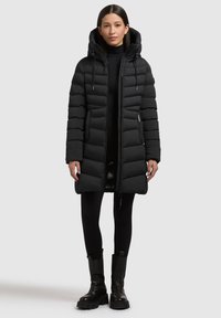 Črna puhasta jakna s kapuco, ki ima vodoravne blazine, sprednji zadrgo in naglavne kvačke. Utežena z v črnimi pajkicami in debelimi čevlji.