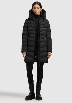 Svart puffjacka med huva, med horisontell quiltning, framtida dragkedja och dragsko-accenter. Matchad med svarta leggings och kraftiga stövlar.