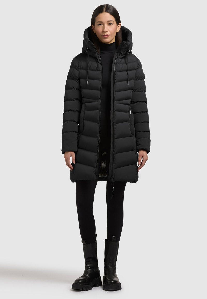 Črna puhasta jakna s kapuco, ki ima vodoravne blazine, sprednji zadrgo in naglavne kvačke. Utežena z v črnimi pajkicami in debelimi čevlji.