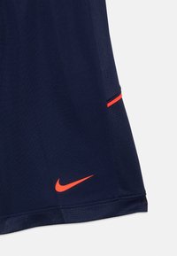 Jūras zila sporta šorti ar sarkano Nike swoosh logo tuvumā apakšmalai un sarkano svītru detaļu uz sānu paneļa.