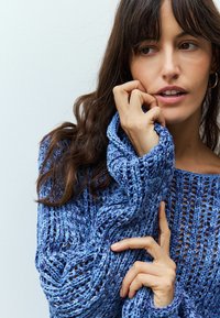 Maglione blu a maglia con un design a trama aperta, caratterizzato da maniche lunghe e un'ampia scollatura. Testurizzato, con tonalità di blu variate.