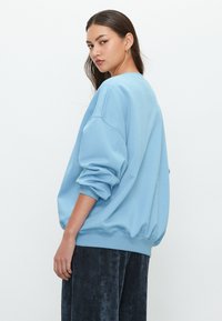 Világoskék, bő fazonú pulóver ballon ujjakkal és bordázott szegéllyel, sötét kordbársony nadrággal párosítva. Sima textúra és laza szabás.