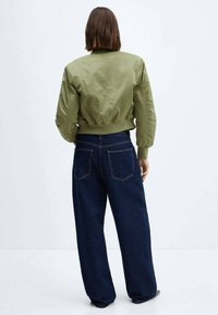 Olivgrüne Bomberjacke mit taillierter Form und gerippten Bündchen, kombiniert mit locker sitzenden dunkelblauen Jeans aus Denim mit Gesäßtaschen.