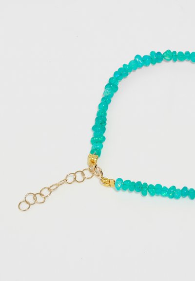 Collana in pietra turchese con perle di forma irregolare, dettagli in metallo dorato e una chiusura con anelli intrecciati per la regolazione.