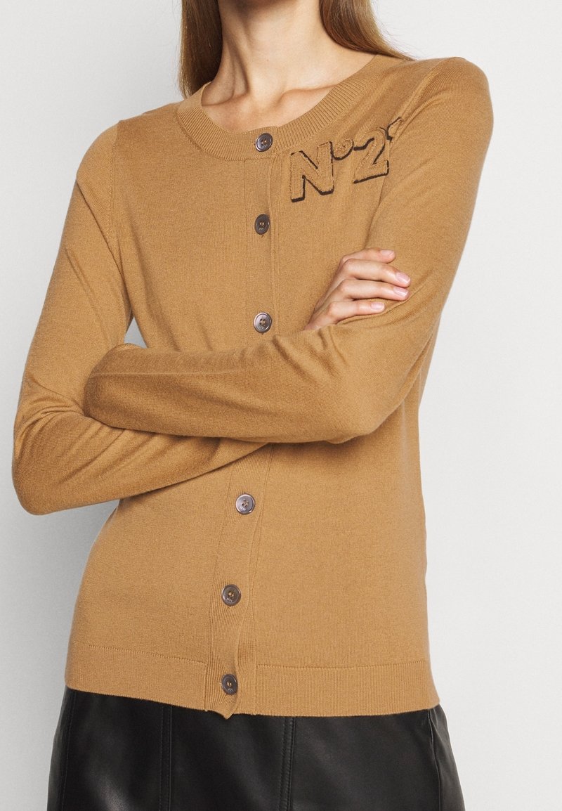 Svetr v barvě velbloudí z měkké látky, s kulatým výstřihem, předními knoflíky a vyšitým detailem "N°21" na hrudi.