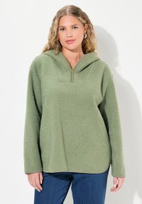 Zielony polarowy sweter z półzasuwanym dekoltem i kapturem. Posiada teksturowaną powierzchnię oraz długie rękawy. Swobodny krój z zaokrąglonym dołem.