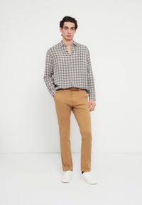 Πουκάμισο με μακριά μανίκια σε καρό γκρι και λευκό με γιακά, συνδυασμένο με στενά παντελόνια καφέ και λευκά αθλητικά παπούτσια. Απλή ζώνη ως διακριτικό στοιχείο.