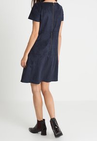 Námořnická modrá, krátký rukáv, šaty s hladkým povrchem a zadním zipem. Nošeno s černými kotníkovými botami s lesklým povrchem.