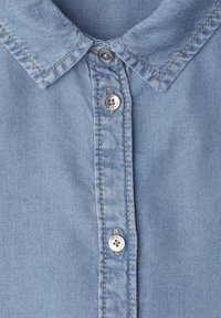 Camisa de mezclilla azul claro con cuello puntiagudo y tres botones metálicos abrochados a lo largo de la tapeta frontal.