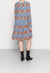 Vestido de manga larga con un patrón floral en azul, naranja y blanco, con falda abullonada; combinado con botas de tacón negras.
