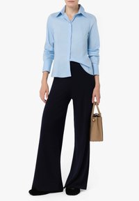 Camicia button-up azzurro chiaro con colletto, abbinata a pantaloni larghi blu navy. Il modello tiene una borsa beige. Tessuto morbido e vestibilità rilassata.