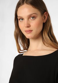 Zwart jurkje met een vierkante halslijn, gladde textuur en korte mouwen, met een getailleerde bodice en eenvoudig ontwerp, dat minimalisme benadrukt.