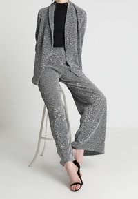 Grå stickad tvådelad outfit bestående av en långärmad cardigan och vida byxor med ett strukturerat mönster, tillsammans med svarta klackar.