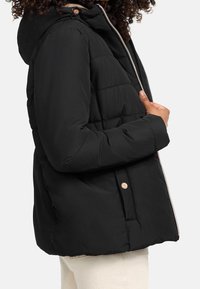 Černá péřová bunda s kapucí, se zipovým zapínáním a patentkami. Tkanina je hladká s horizontálně prošívanými sekcemi.