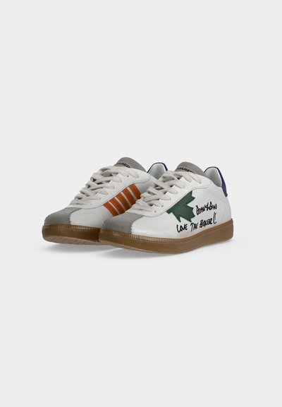 Paire de baskets basses blanches avec semelles en gomme, bouts gris, un côté présente des rayures orange, l'autre côté une flèche verte et un texte noir.