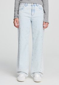 Jeans a gamba larga di un blu chiaro con decorazioni di strass sparse, presentano un classico design a cinque tasche e una chiusura con bottone.