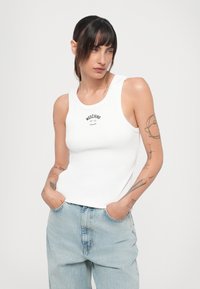 Valge soonikuline särgike, millel on ümmargune kaelus ja trükitud "Moschino" logo. Koos helesiniste, vabalt istuvate teksadega.