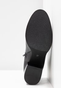 Botte noire avec une tige en cuir lisse, semelle en caoutchouc texturée, détail discret de couture et marquage de taille (37) sur le côté de la semelle.