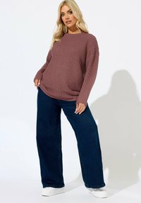 Wafflestickad, mauvafärgad tröja med långa ärmar och rund halsringning, i kombination med vida mörk denimjeans och vita sneakers.