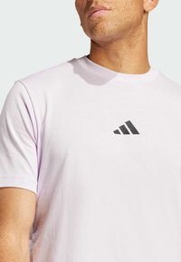 Světle fialové bavlněné tričko s černým logem Adidas se třemi pruhy uprostřed na hrudi. Kulatý výstřih a krátké rukávy.