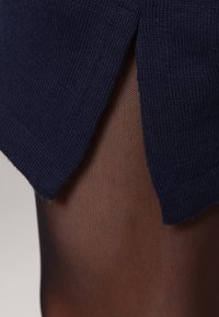 Mörkblå stickad tröja med sidospalt, tillsammans med genomskinliga svarta fisknätsstrumpbyxor som visar ett texturerat mönster.