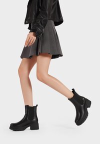 Botines negros de cuero suave, con paneles laterales elásticos, un tacón grueso y una lengüeta en la parte posterior.