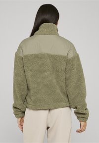 Zaļa, pārlielu izmēru jaka ar pūkainu, teksturētu apakšdaļu un gludu augšējo paneli. Augsts apkaklis, plati piedurknes un elastīgs apakša.