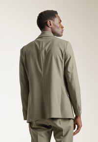 Blazer de color verde oliva con un diseño estructurado, tejido texturizado, solapa de muesca y cierre de un botón, que presenta un ajuste slim y una silueta entallada.