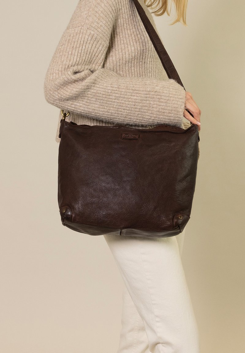 Brown leather shoulder bag with a soft, textured finish. Features a long strap, subtle branding, and rounded bottom corners.