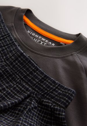 Tumma harmaa collegepaita, jossa oranssi yksityiskohta kauluksessa. Vasemmalla puolella teksturoitu laivastonsininen kangas, jossa ruudullinen kuvio.