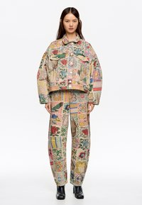 Conjunto de chaqueta y pantalones de mezclilla con un diseño colorido, floral y estampado. La chaqueta tiene grandes bolsillos frontales y un corte holgado.