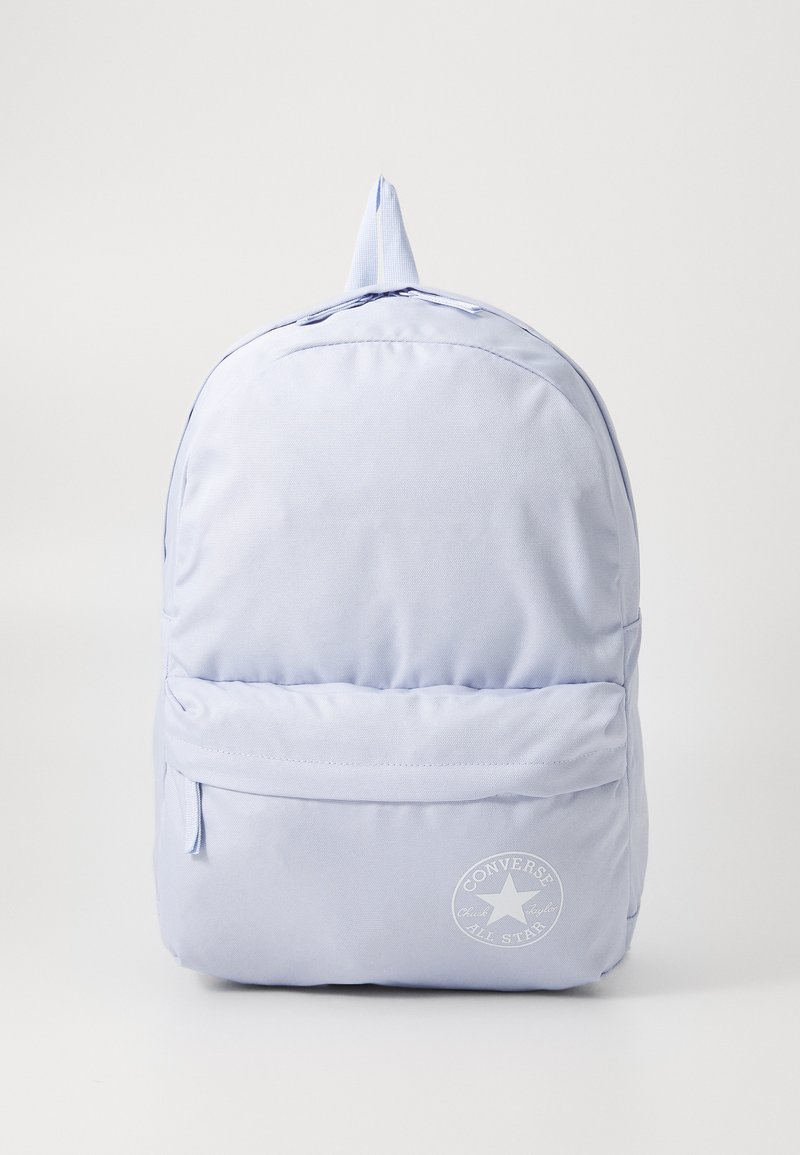 Mochila azul claro feita de tecido durável, com um bolso frontal, alça no topo e detalhe em forma de logotipo circular na frente. Textura suave, design casual.