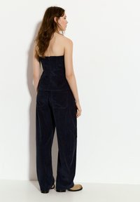 Temno modra kordurasta brezramna bluza s oprijetim korpusom, v kombinaciji z širokimi kordurastimi hlačami z zadnjimi žepi in teksturiranim materialom.