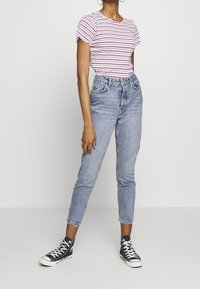 Červené a bílé pruhované tričko s krátkým rukávem a volánkovými okraji, spárované se světle modrými džíny s vysokým pasem a černými teniskami.