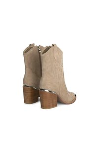 Beżowe zamszowe botki za kostkę z detalicznym szyciem, spiczastym noskiem, ozdobnymi pętelkami do zakupu oraz brązowym drewnianym obcasem blokowym z chromowanymi akcentami.