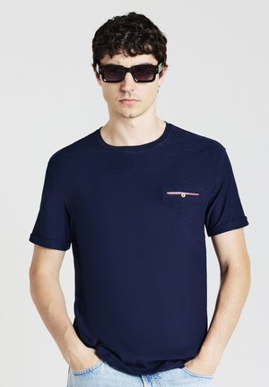 T-shirt bleu marine en tissu doux, col rond, avec des manches courtes retroussées et une petite poche poitrine avec un détail en bandes rouges et blanches.