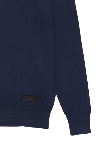 Maglione blu navy con collo a giro, polsini a coste e un'etichetta di marca nera testurizzata sul lato sinistro in basso. Materiale in morbido misto cotone.