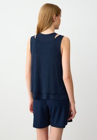 Marineblauwe mouwloze top met gelaagde zoom en blootgestelde schouderbanden, gecombineerd met bijpassende shorts, gemaakt van zachte, lichte stof.