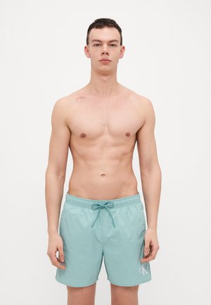 Light blue swim shorts made of a smooth, lightweight fabric. Features an elastic waistband with a drawstring, and a subtle logo detail.