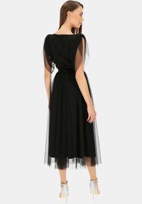Czarna midi sukienka z przezroczystymi rękawami, dopasowanym talią i luźną spódnicą. Teksturowany materiał i subtelny połysk, w połączeniu z srebrnymi obcasami.