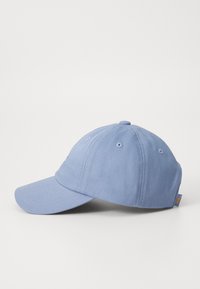 Boné azul claro com aba curva, feito de tecido de algodão, apresentando ilhós de ventilação e uma pequena etiqueta com o logótipo de um lado.