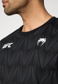 Μαύρο αθλητικό μπλουζάκι με υφασμένο μοτίβο φύλλου, στρογγυλή λαιμόκοψη και λευκές λεπτομέρειες με το λογότυπο UFC στο στήθος.