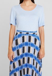 Maglione azzurro chiaro a maniche corte abbinato a una gonna plissettata con audaci motivi a righe blu, neri e beige, con vita elasticizzata.