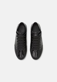 Schwarze Sneaker mit glänzender, lackierter Oberfläche, runden Schnürsenkeln, silbernen Ösen und einem strukturierten seitlichen Design.