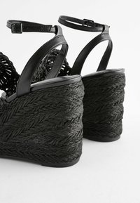 Schwarze Wedgesandalen mit gewebten Seilabsätzen, einem strukturierten schwarzen Obermaterial und verstellbaren Knöchelriemen für einen sicheren Sitz.
