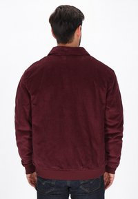 Bordaux velourjakke med krave, elastiske manchetter og talje. Har en struktureret overflade og et ensfarvet design.