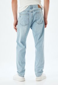 Ljusblå denimjeans med en avslappnad passform, som har två bakfickor och en tanfärgad läderlapp vid midjan, kombinerat med vita skor.